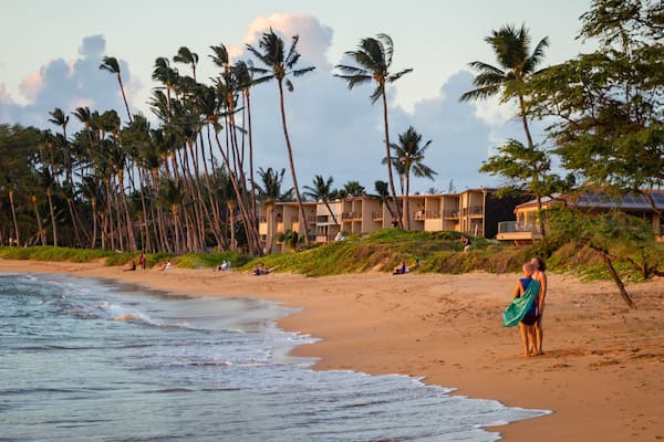 A beach with palm trees, ocean waves, and beachfront buildings.