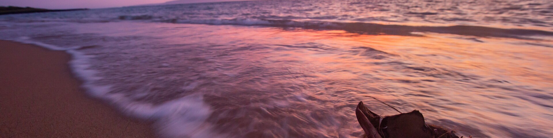 A beach at sunset with waves gently lapping the shore and a boat on the sand.