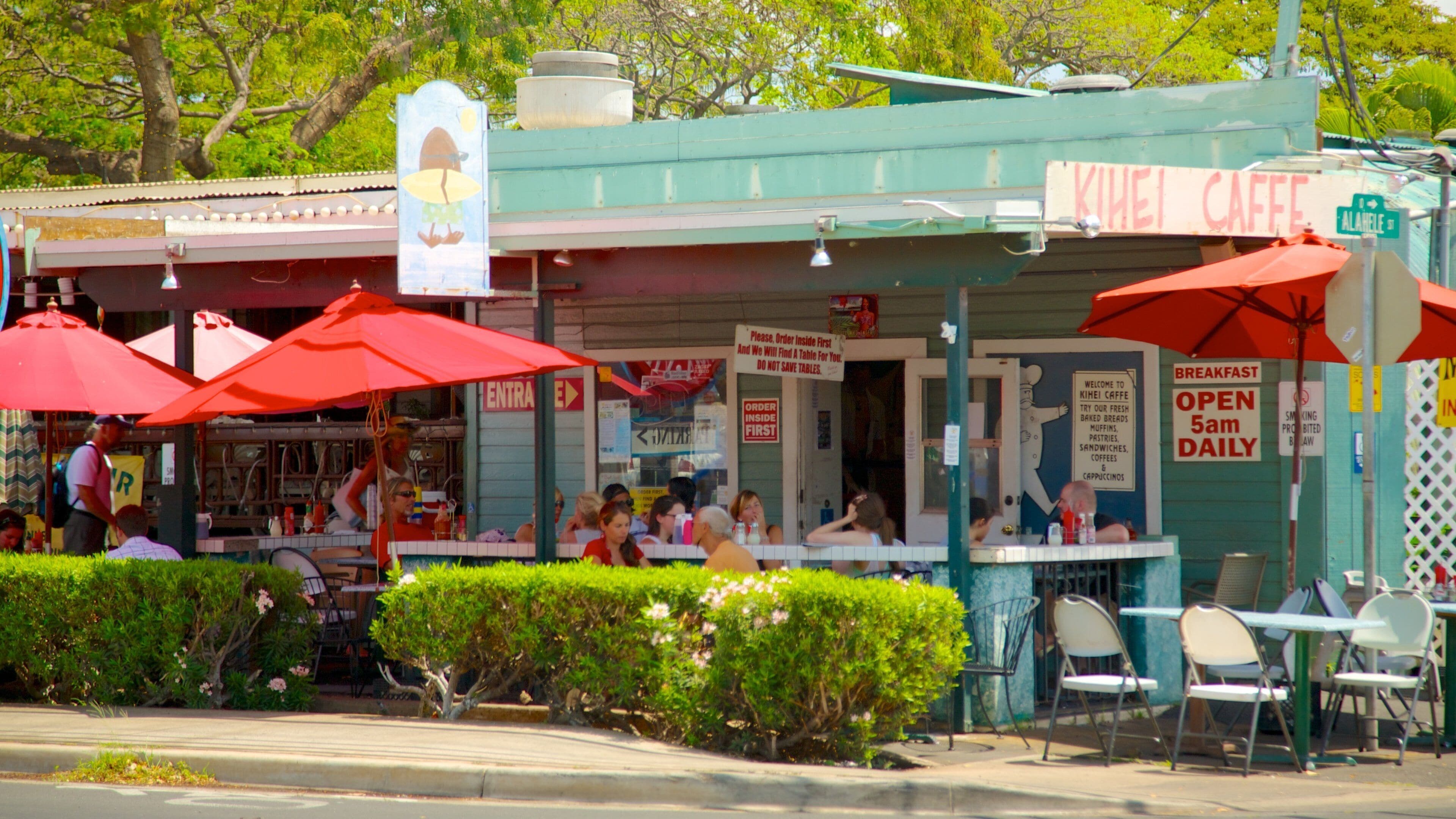 A cafe with outdoor seating, red umbrellas, and a sign that reads "KHEI CAFFE".