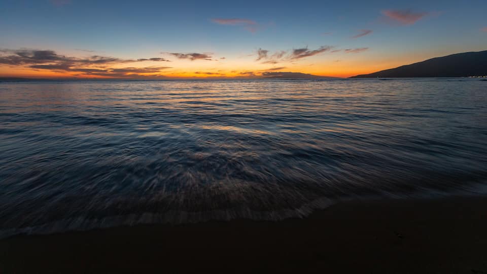 A sunset over a calm sea with gentle waves and a clear sky.