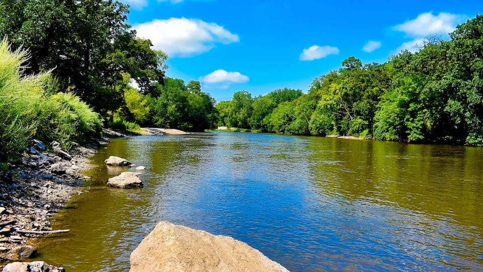 A river with clear water, surrounded by lush green trees and rocks.