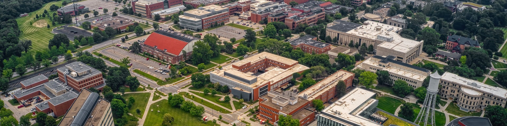 An aerial view of a university campus with multiple buildings, green spaces, and a large parking area.