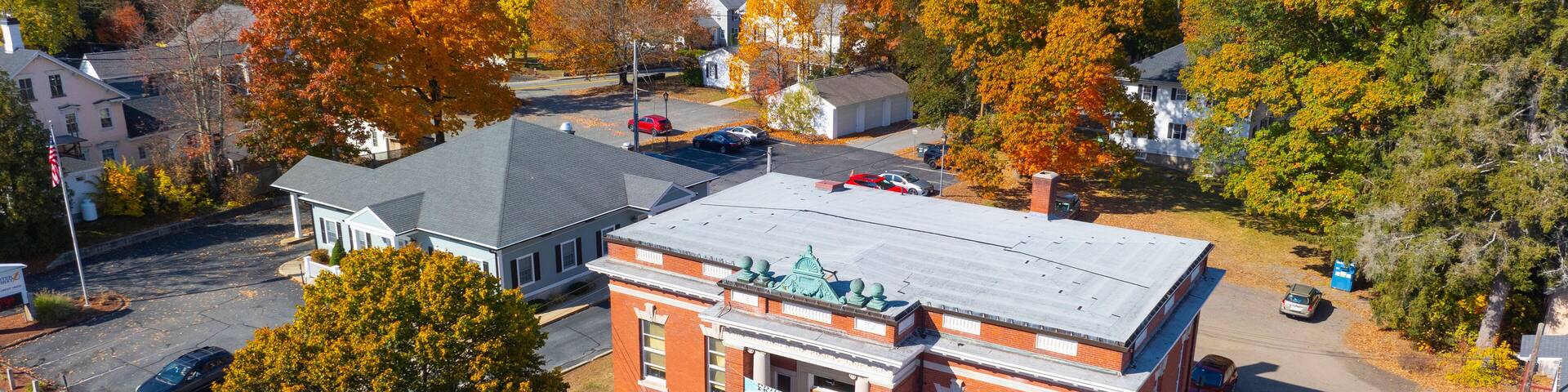A town with autumn-colored trees, a prominent red brick building, and a clear blue sky.