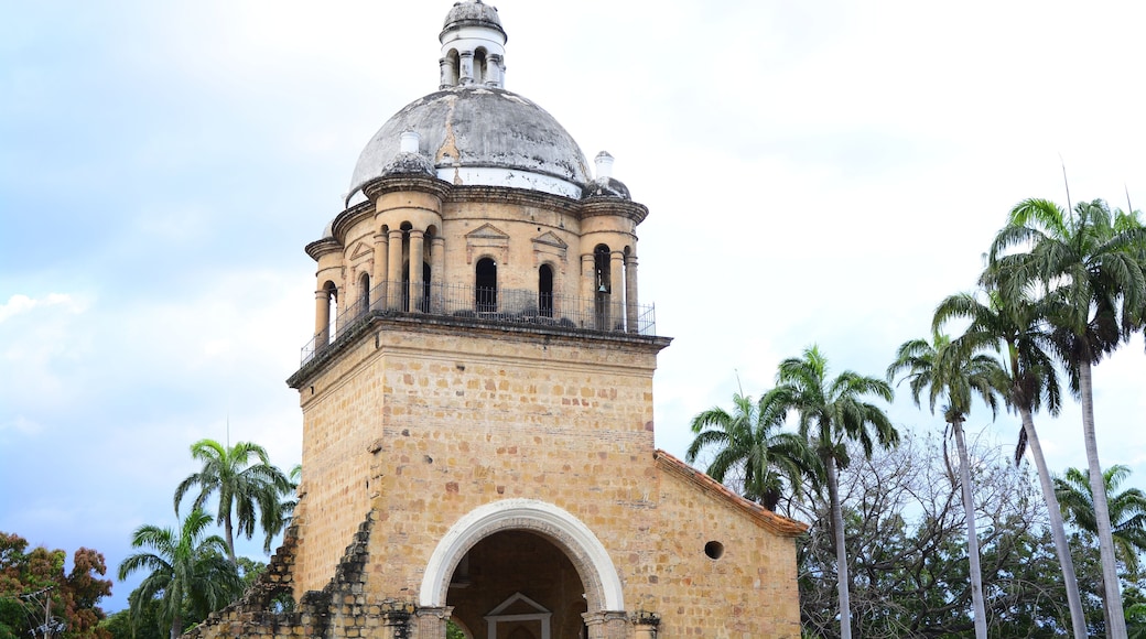 Una torre de piedra histórica con cúpula y campanario, rodeada de palmeras.