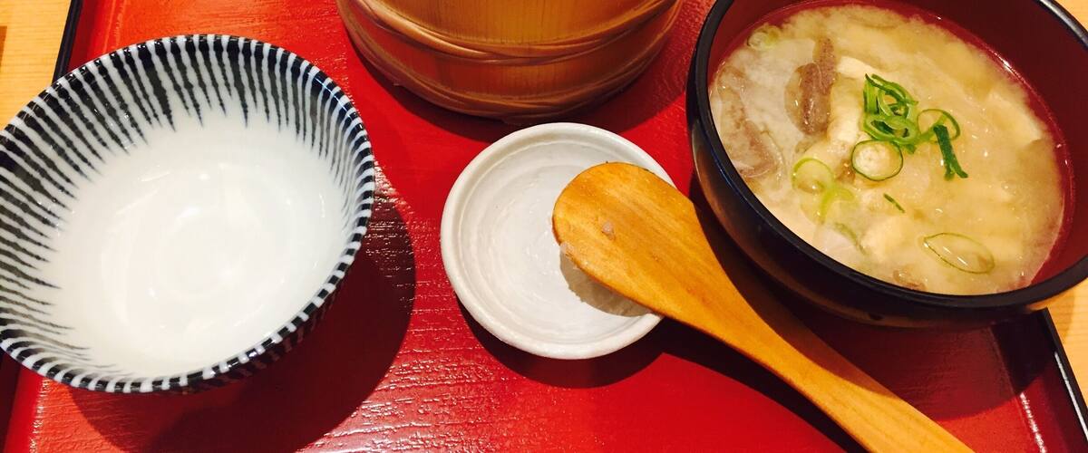 A wooden bowl with a white sauce, a small white dish, and a bowl of soup with green onions.