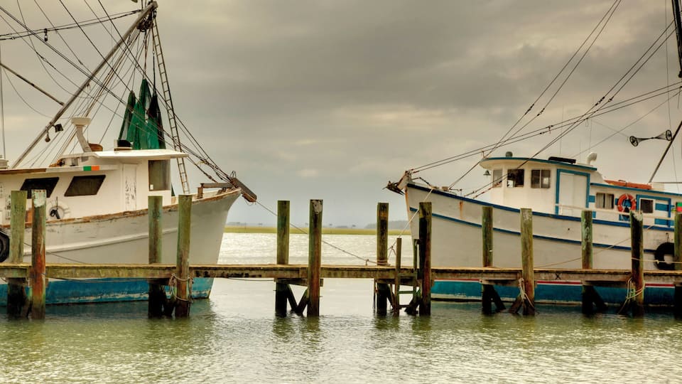 Two boats docked at a pier with a cloudy sky in the background.