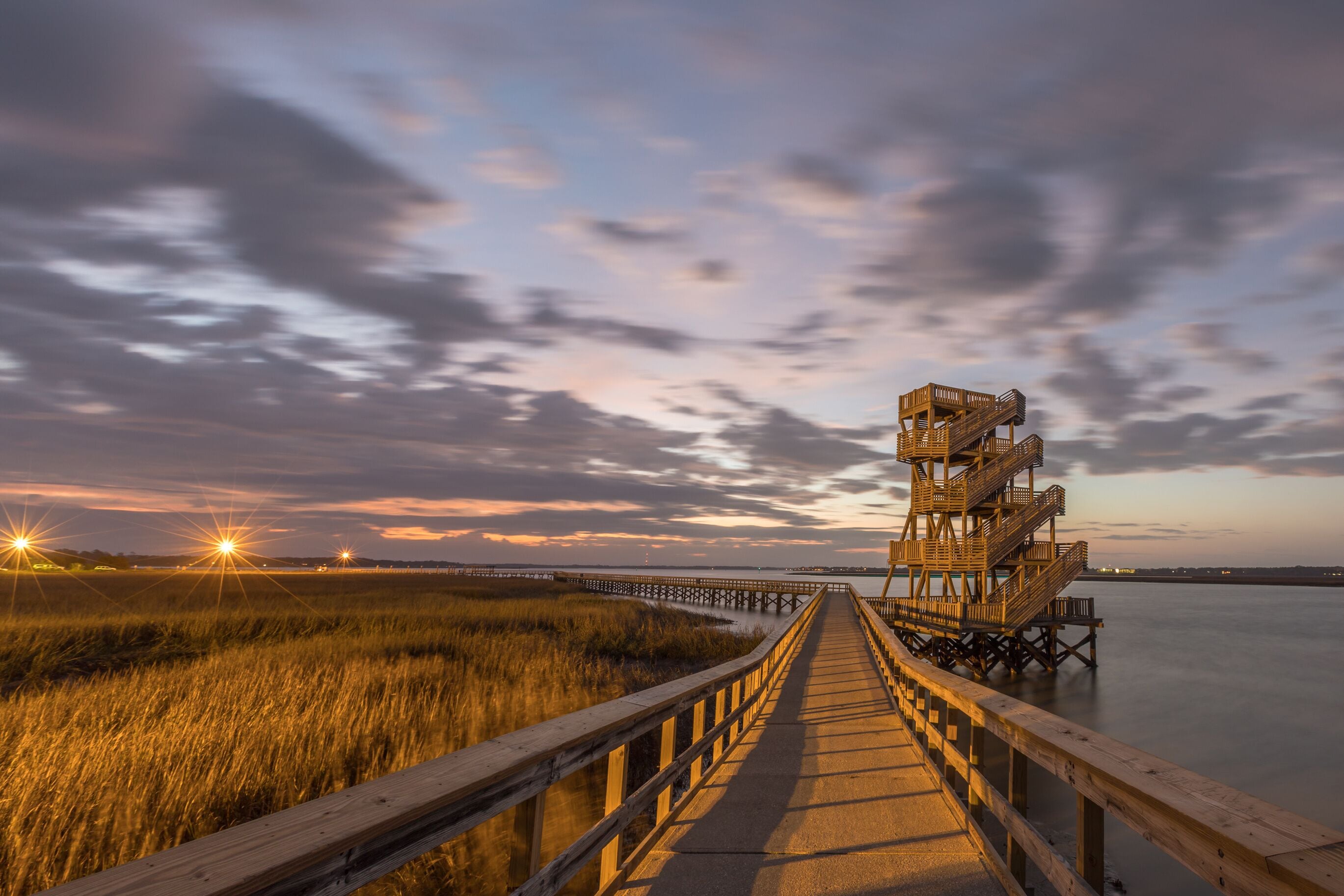 A wooden pier leading to a lighthouse at sunset.