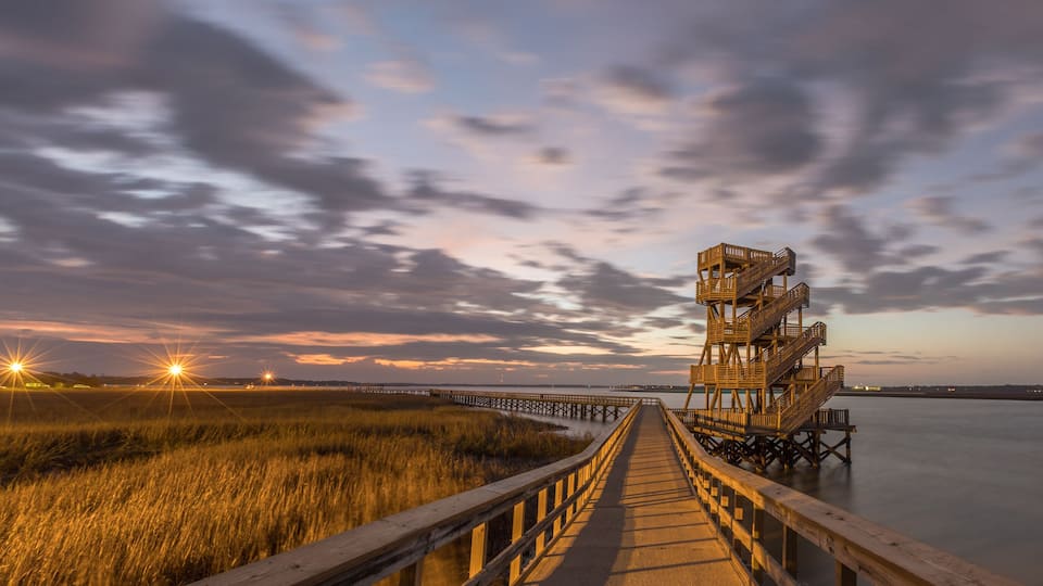A wooden pier leading to a lighthouse at sunset.