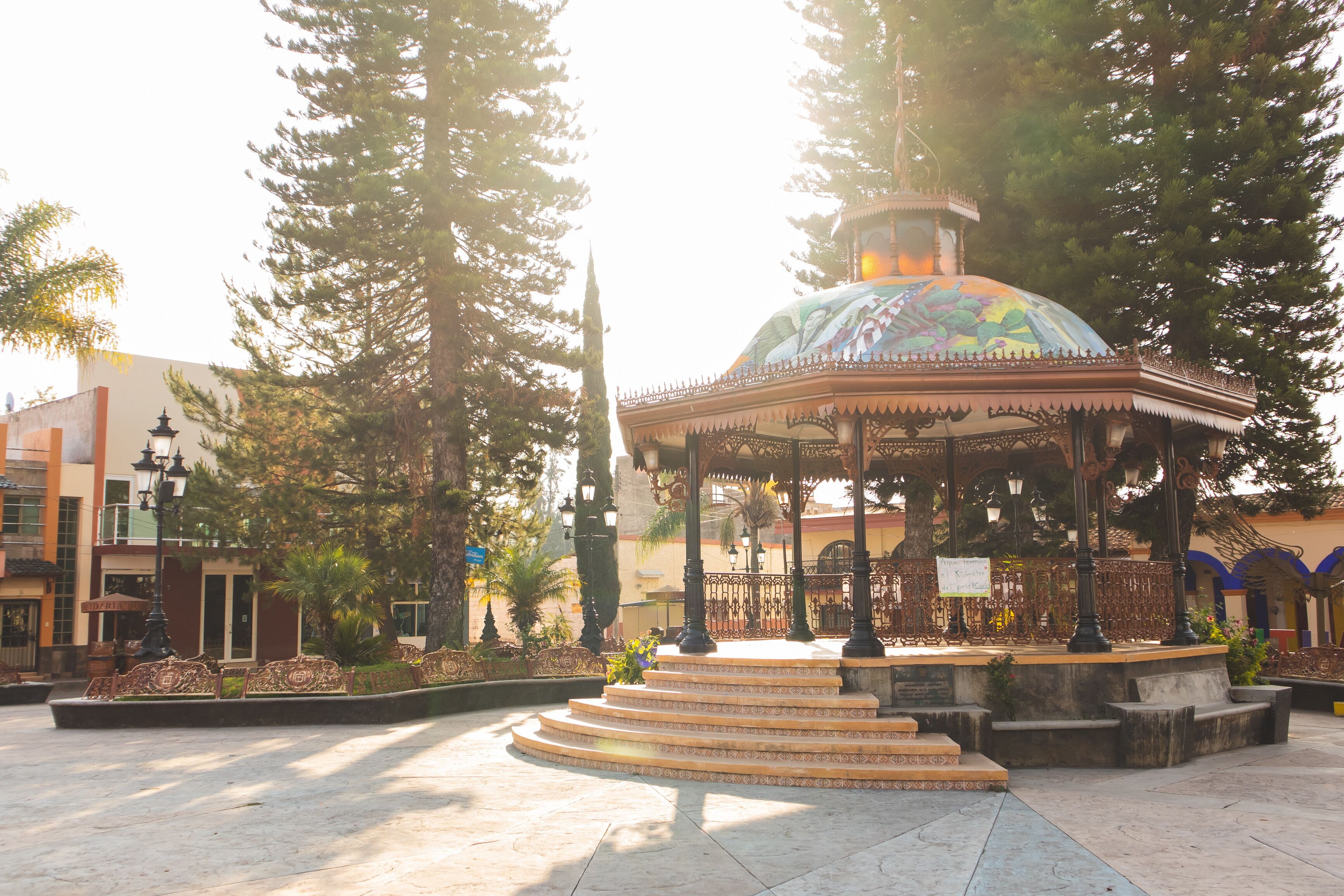 A gazebo with a colorful dome, surrounded by trees and a tiled plaza.