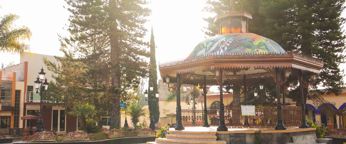 A gazebo with a colorful dome, surrounded by trees and a tiled plaza.