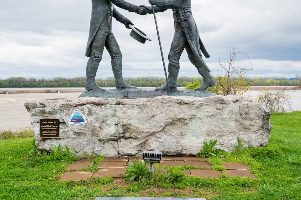 Una estatua de dos figuras estrechándose las manos sobre una roca, con una placa debajo.
