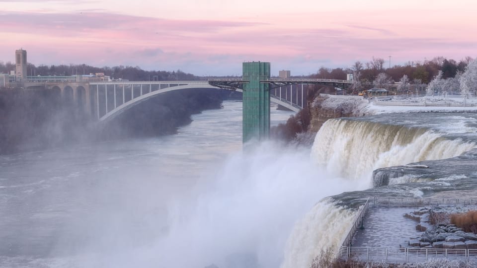 A waterfall with a bridge, a cityscape, and a snowy park.