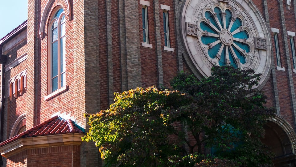 A historic brick building with a large circular stained glass window and arched windows.