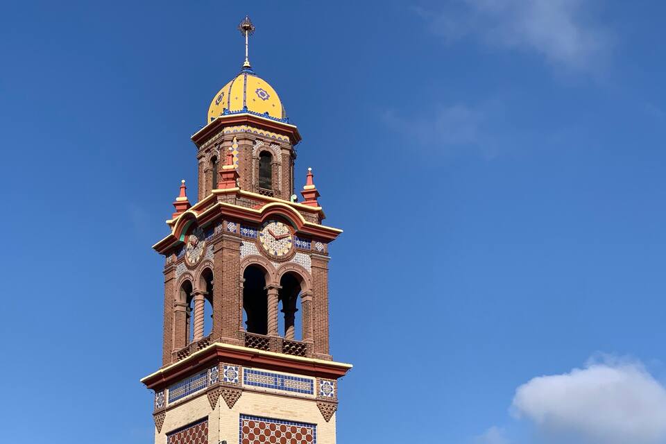 A clock tower with a yellow dome and intricate tile work against a clear blue sky.