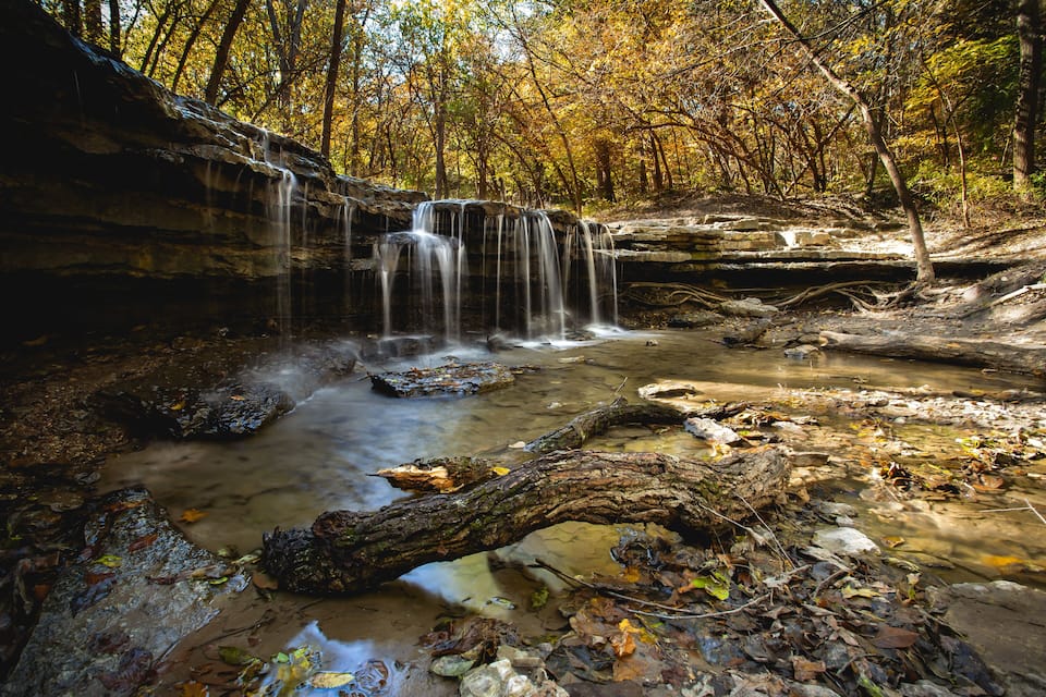 A waterfall in a forest with autumn leaves.