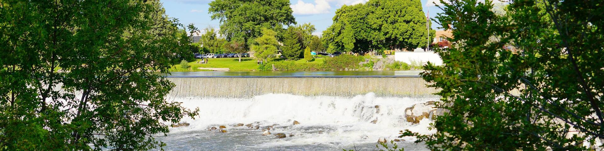 A river with a dam, surrounded by trees and a park.