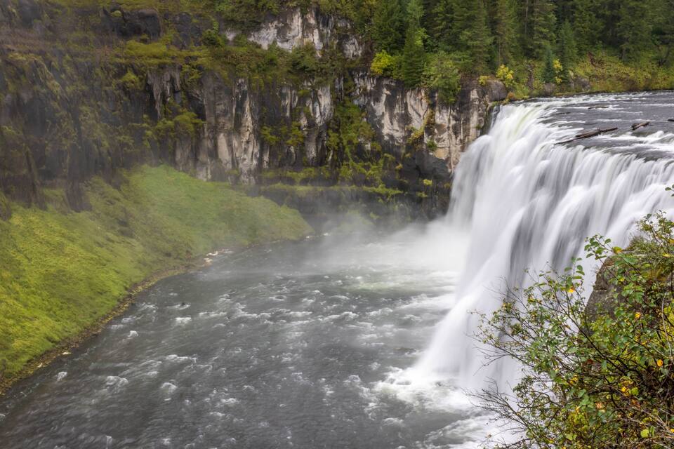 A waterfall cascading down a rocky cliff surrounded by lush greenery.
