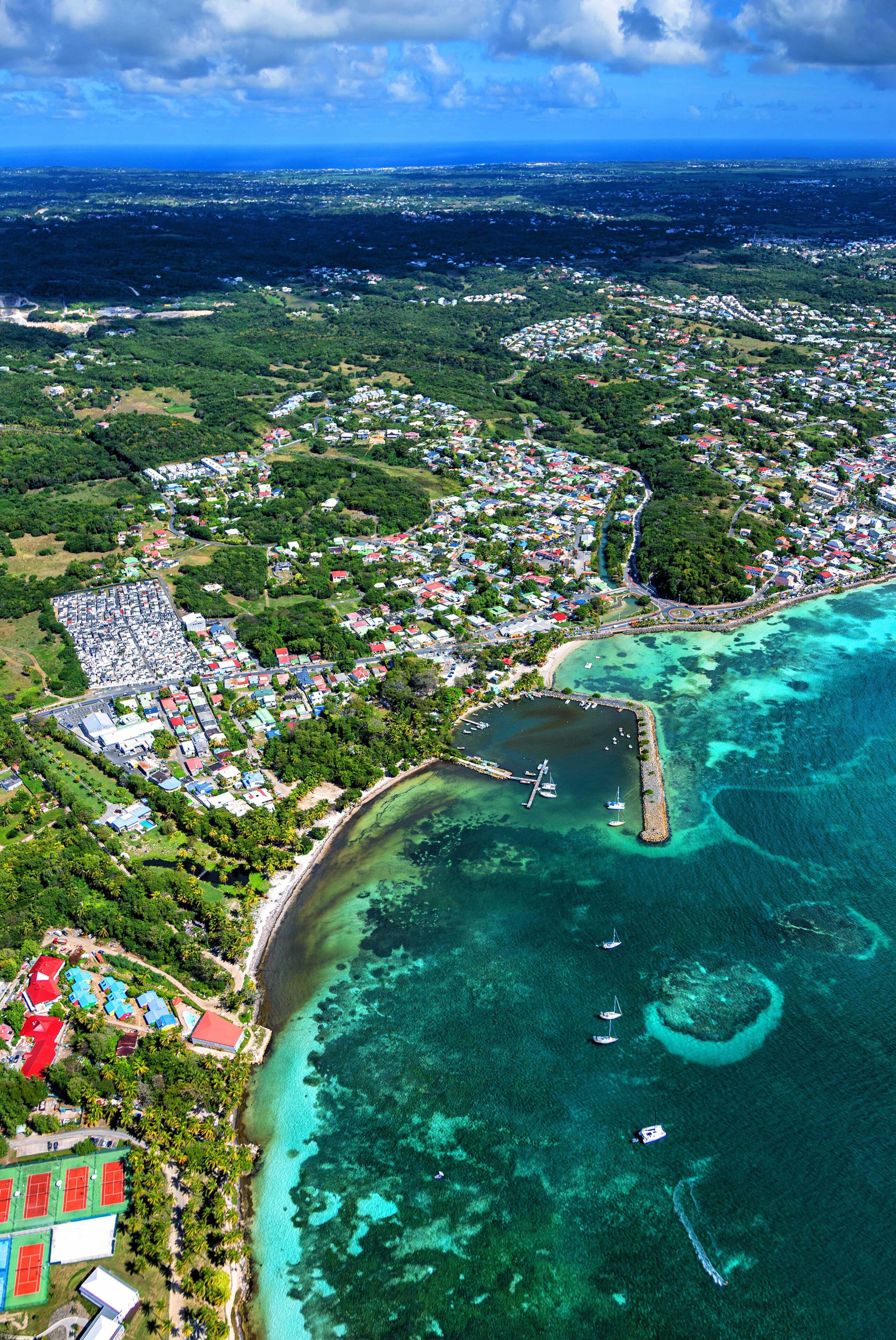 An aerial view of a coastal town with a marina, clear blue waters, and lush greenery.
