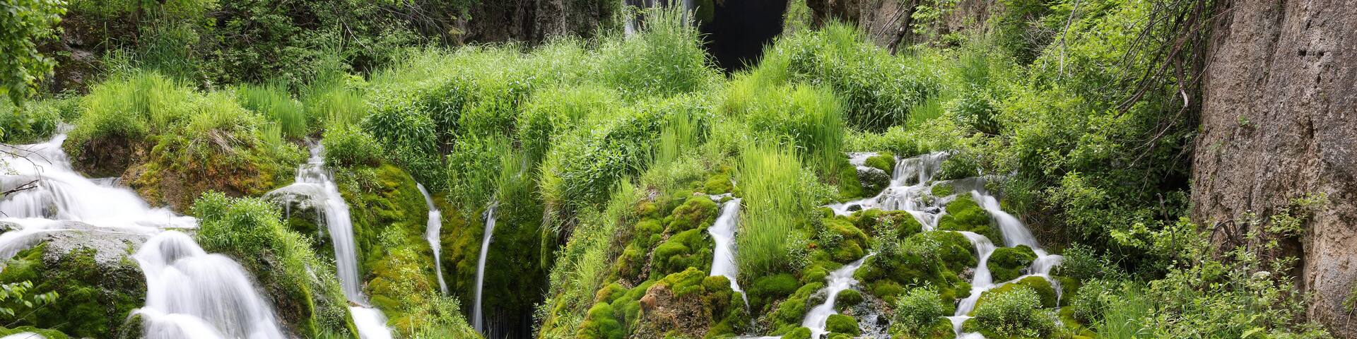Un paisaje verde exuberante con varias cascadas que se precipitan sobre rocas cubiertas de musgo y vegetación densa.