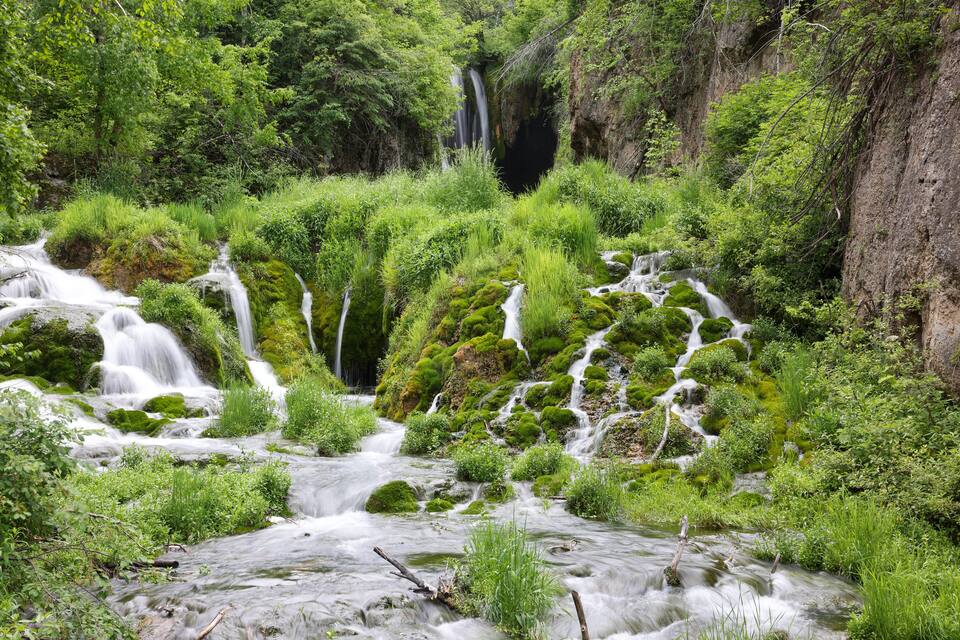 Un paisaje verde exuberante con varias cascadas que se precipitan sobre rocas cubiertas de musgo y vegetación densa.