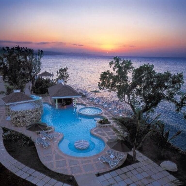 A resort pool with a sunset view, lounge chairs, and a gazebo.