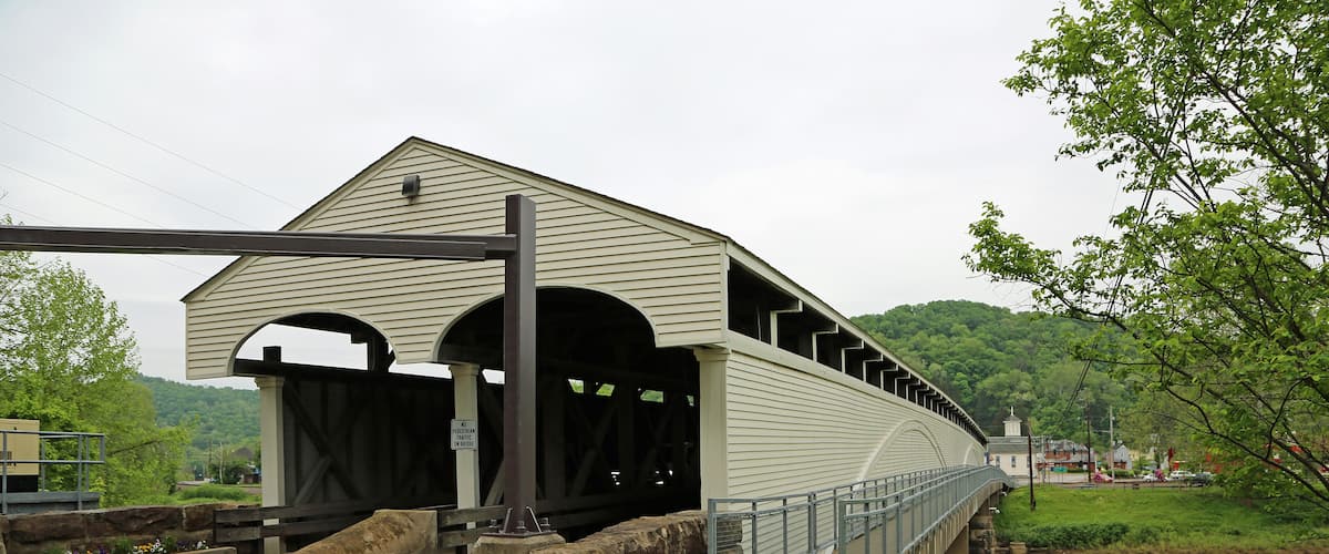 A covered bridge over a river with a grassy area and trees nearby.