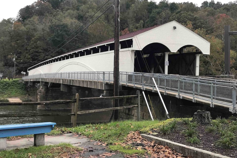 A covered bridge with a white exterior and a red roof, spanning over a river.