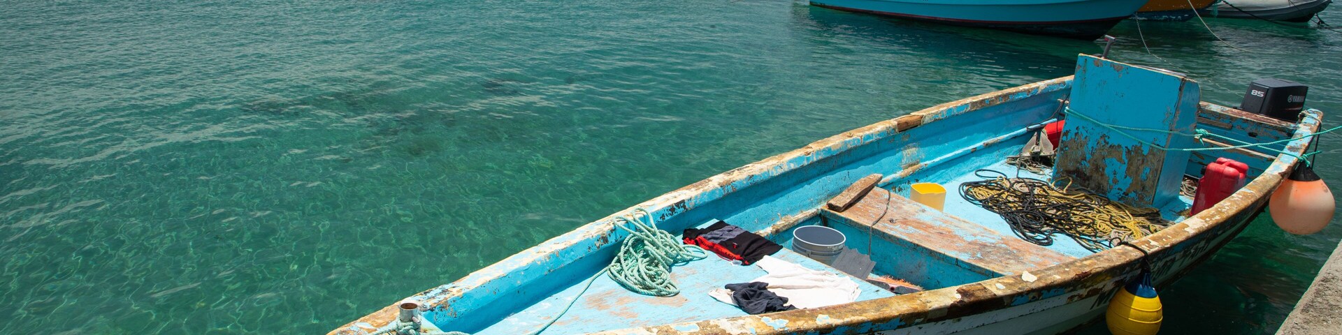 Una pequeña embarcación con casco azul y blanco amarrada en un muelle.