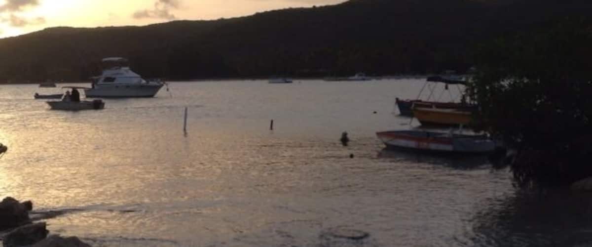 A sunset over a calm body of water with boats and a rocky shoreline.
