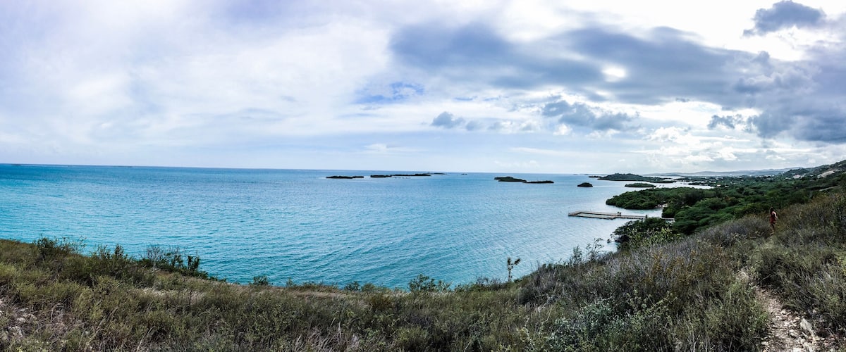 A coastal landscape with a clear blue sea, rocky outcrops, and a distant island.
