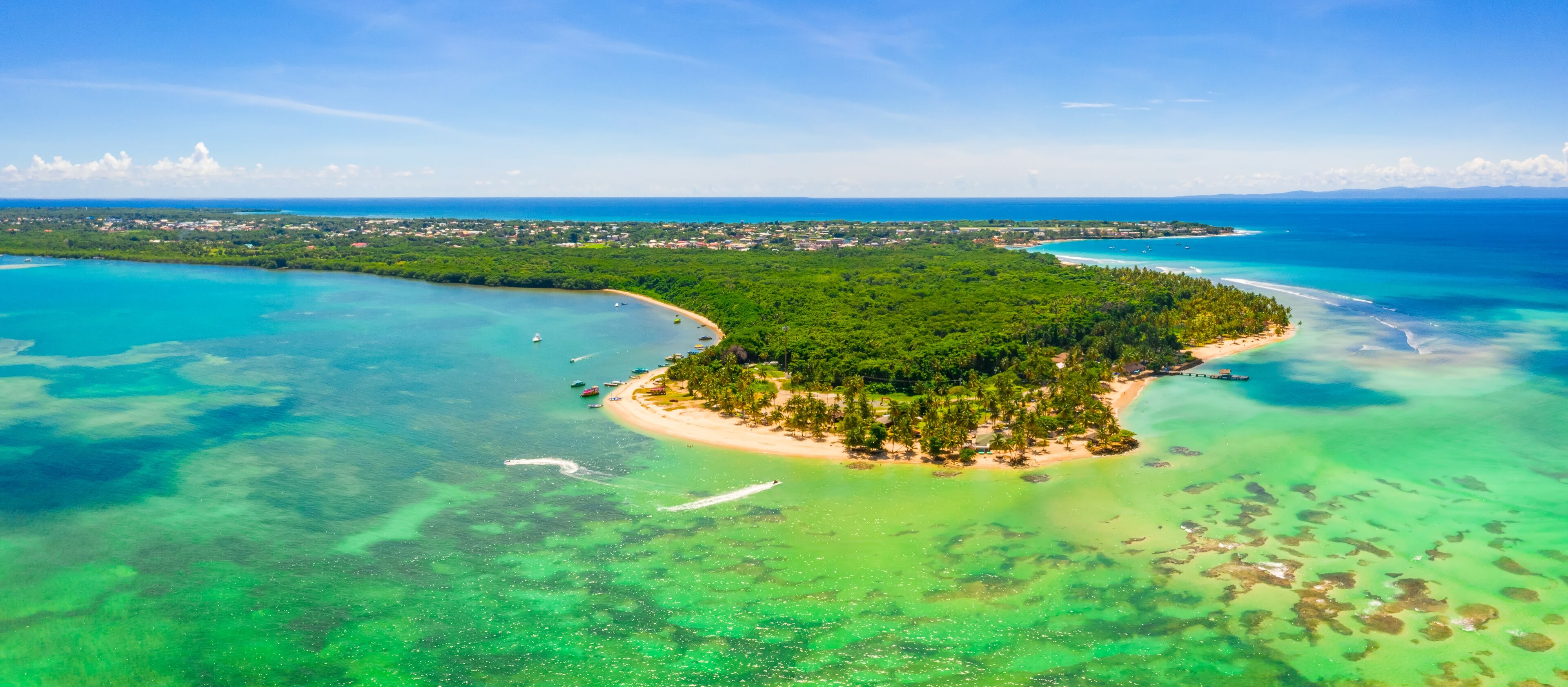 An aerial view of a tropical island with clear turquoise waters, a sandy beach, and dense green vegetation.