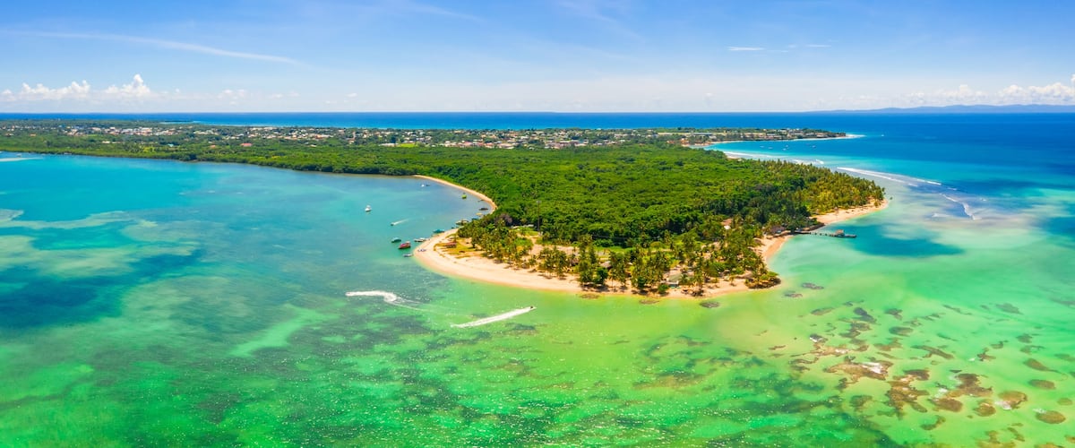 An aerial view of a tropical island with clear turquoise waters, a sandy beach, and dense green vegetation.