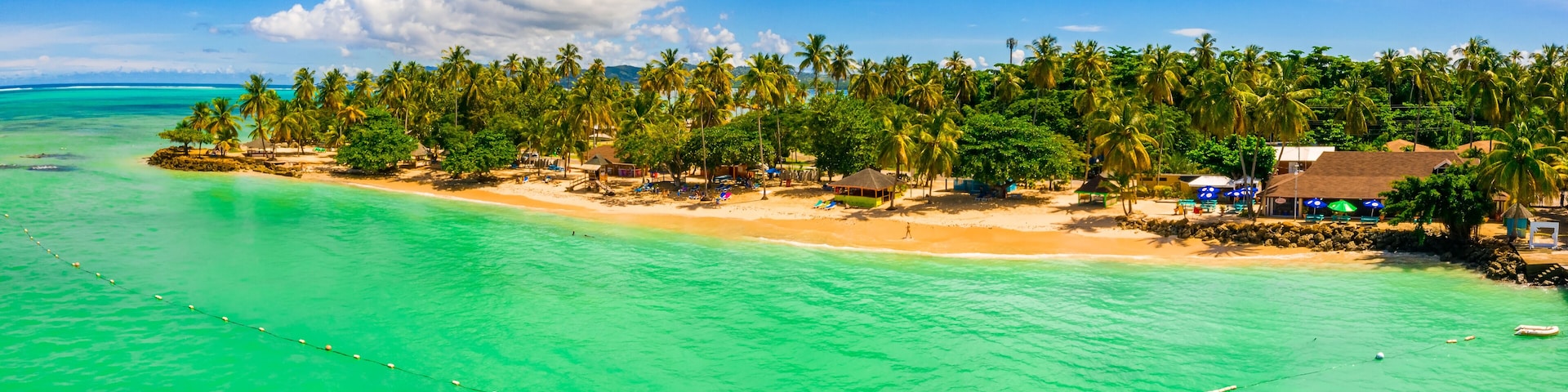 A tropical beach with clear turquoise waters, palm trees, and small huts.
