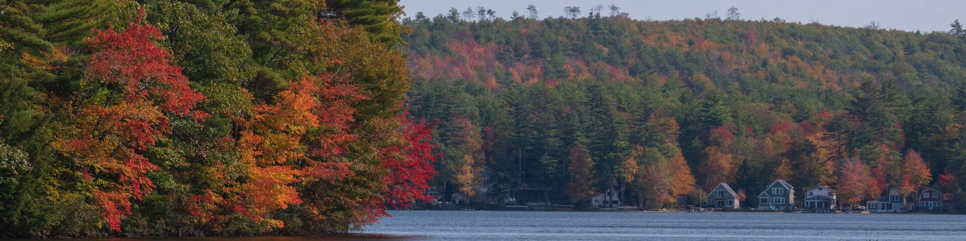 A lake with autumn foliage, a dock, and houses on the shore.