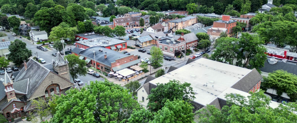 aerial view of rhinebeck new york (hudson valley small town next to catskill mountains) trees main street homes businesses houses (residential and commercial downtown area) drone looking down sunset