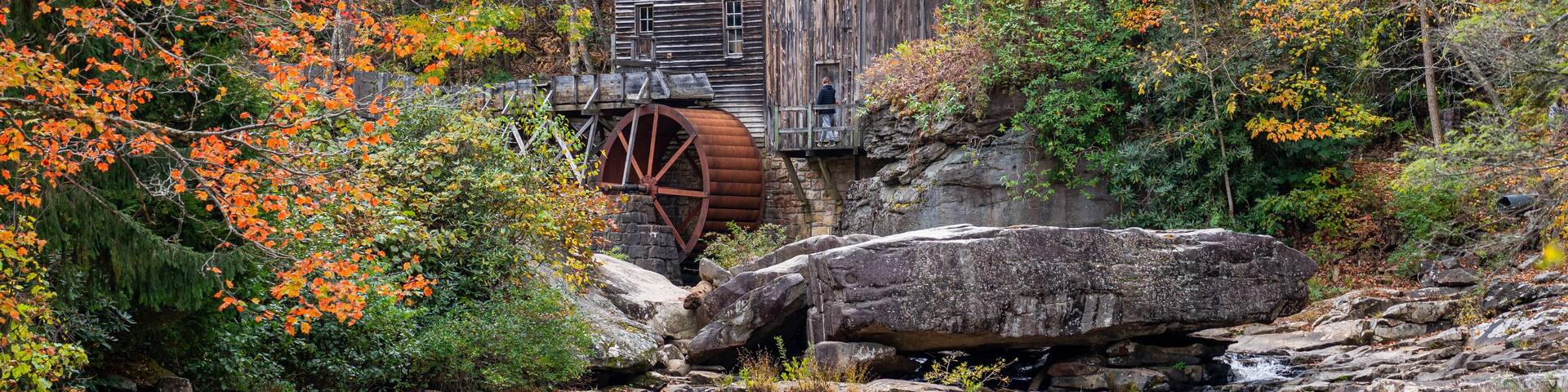 A wooden watermill surrounded by autumn foliage.
