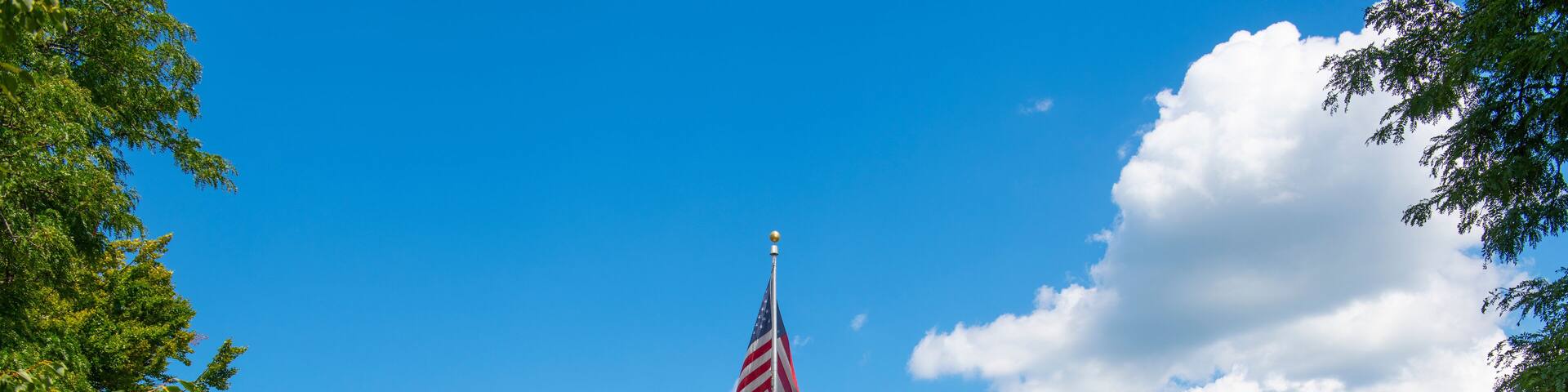 A historic building with a prominent tower, surrounded by lush green lawns and a flagpole with an American flag.