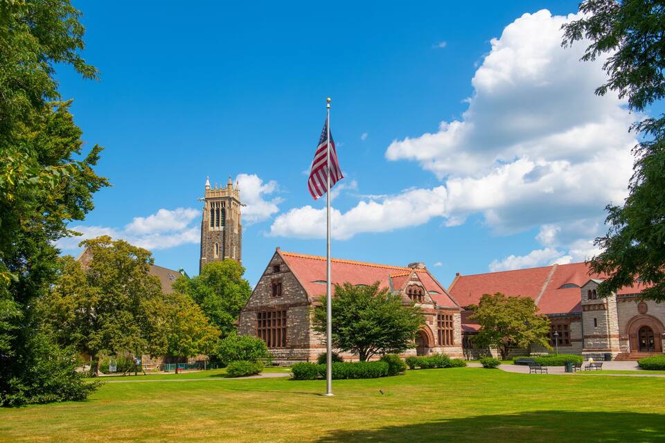 A historic building with a prominent tower, surrounded by lush green lawns and a flagpole with an American flag.