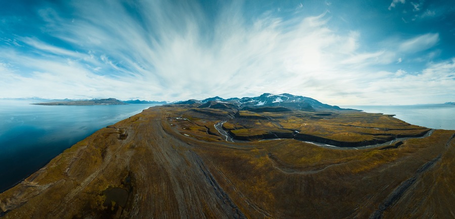 a shot from a drone of breathtaking footage of wild nature in Svalbard, majestic mountains in the clouds, a mighty river and nature under the cloud, a frozen glacier in the middle of the mountains,