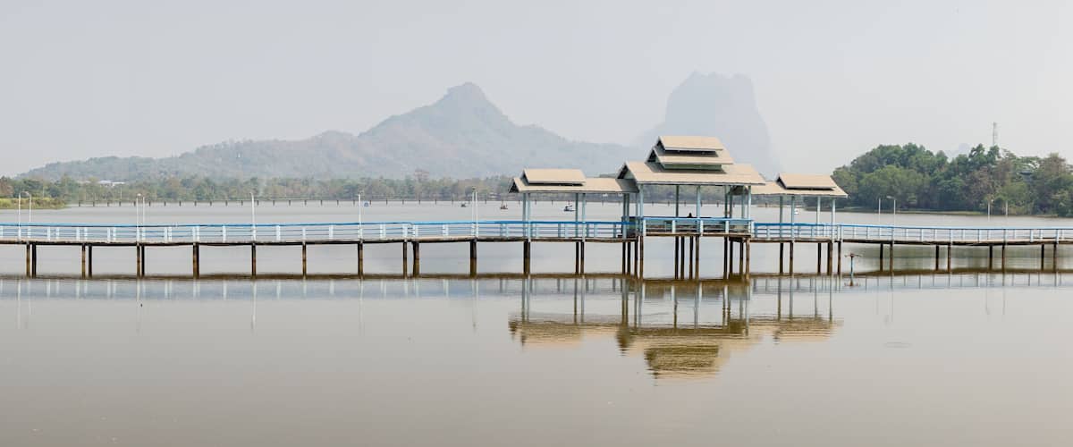 A calm lake with a wooden pier extending into the water. In the background, there is a mountain and a forested area.