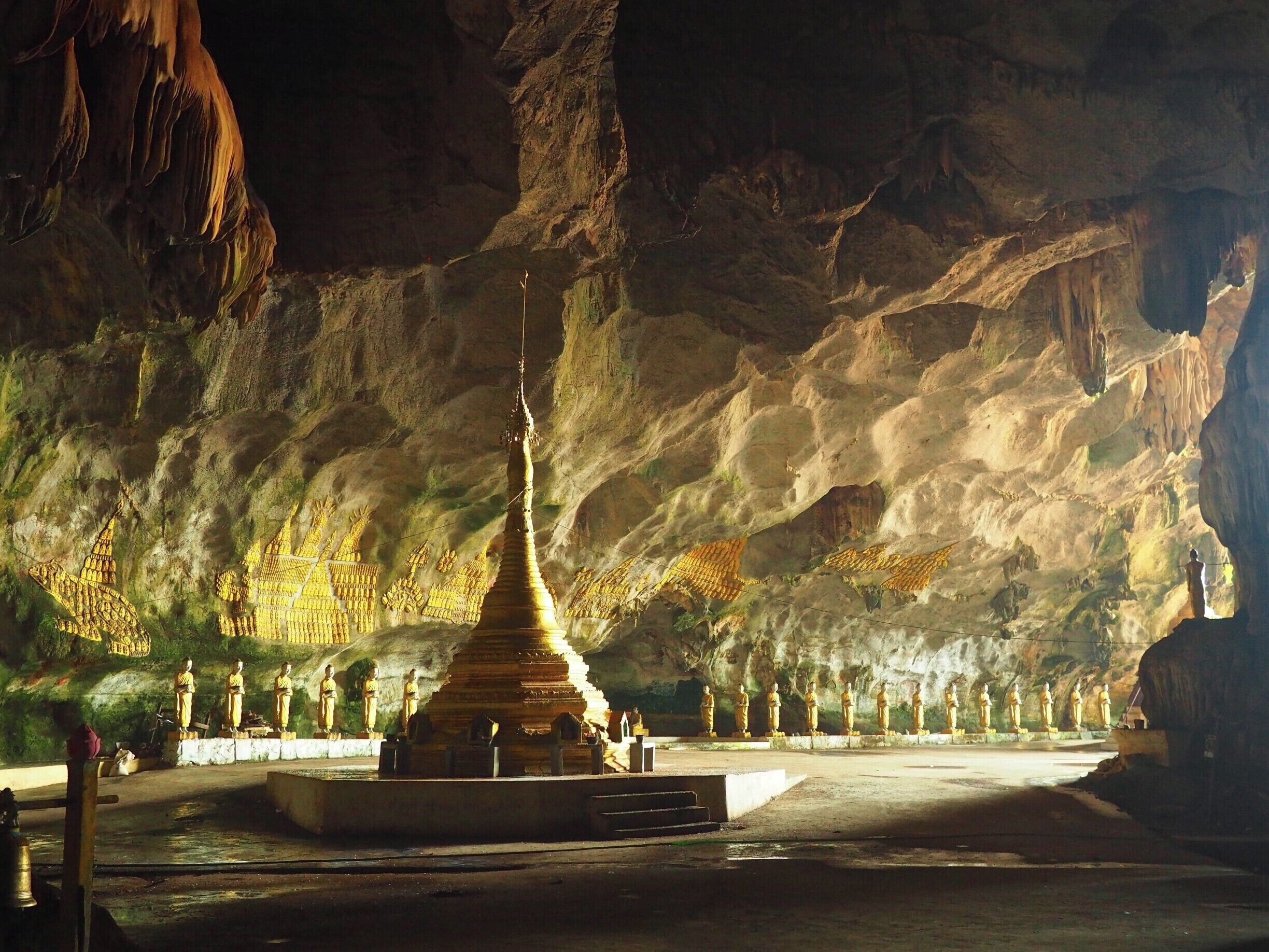 A cave temple with golden statues and a central stupa.