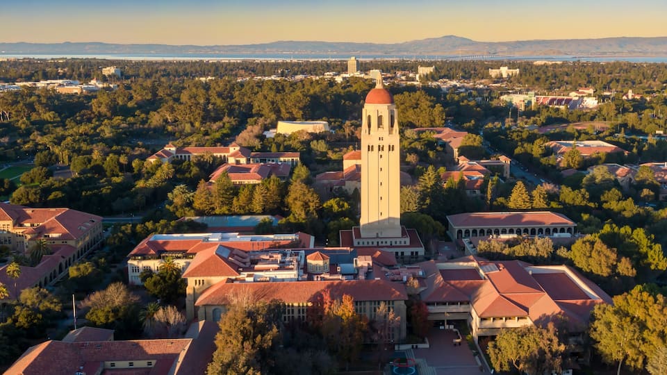 A university campus with a prominent clock tower, surrounded by trees and buildings with red-tiled roofs.