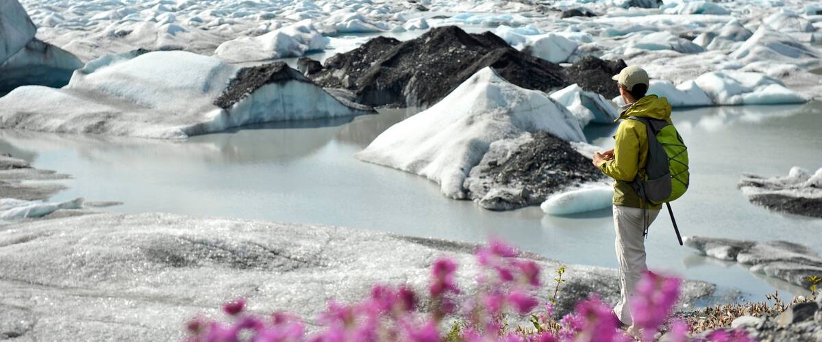 A person standing on a glacier with icebergs and mountains in the background.