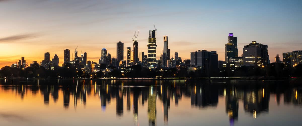 Une vue sur les gratte-ciel d’une ville au crépuscule, avec leurs reflets dans une étendue d’eau calme.