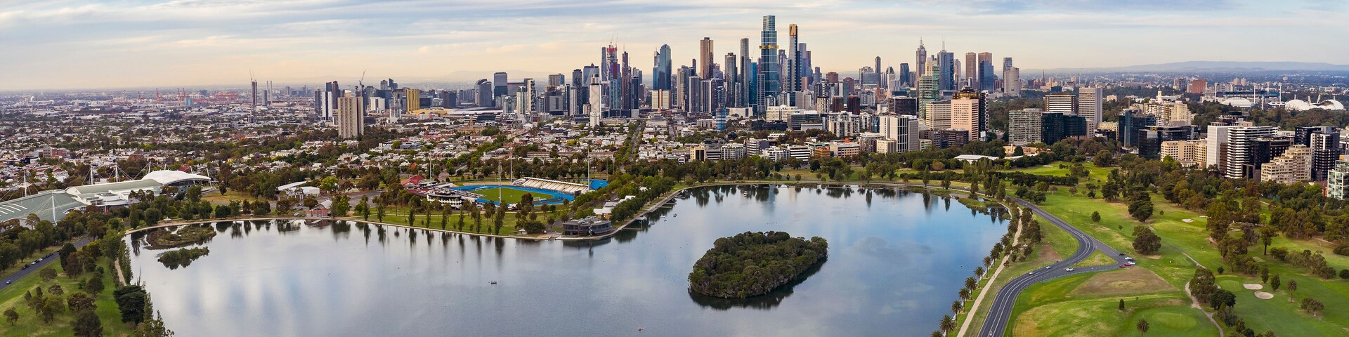 Un horizonte urbano con una extensa masa de agua, un parque con un lago y un estadio.