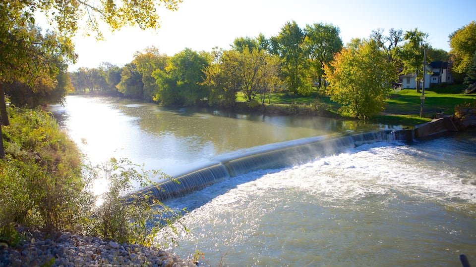 A river with a dam and waterfall, surrounded by trees and a grassy area.