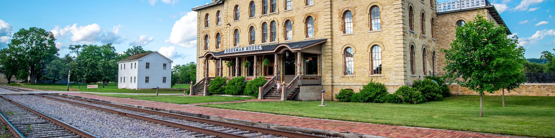 A historic building with a sign reading 'DOUSMAN HOUSE' in front of a railway track.