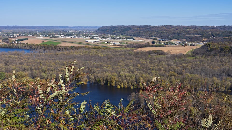A lake surrounded by dense forest and fields, with a town in the background.