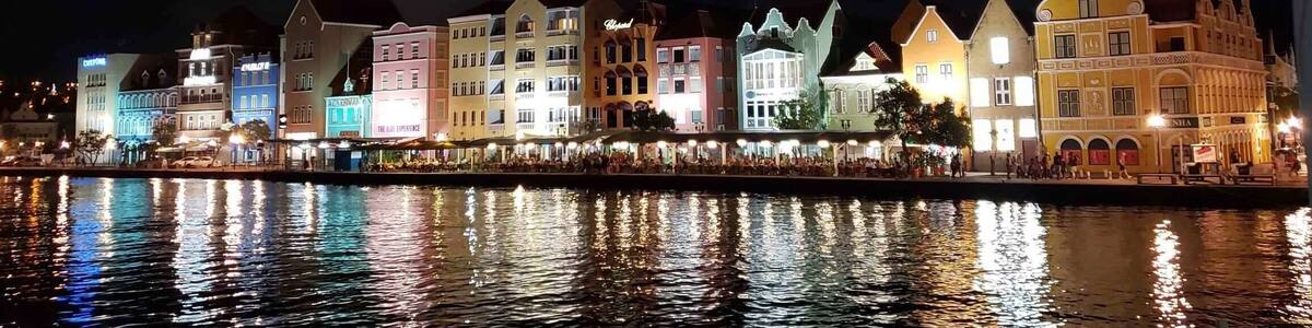 A waterfront with colorful buildings reflecting on the water, a full moon in the sky, and a clear night sky.