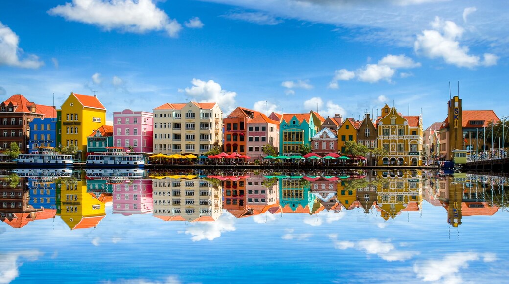 Uma orla com edifícios coloridos refletidos na água, céu azul límpido e mar calmo.